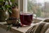 A glass mug of deep red elderberry tea on a rainy windowsill